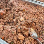 A batch of homemade dog food in red-lidded containers, filled with fresh meats, vegetables, and supplements for a healthy pup’s diet.