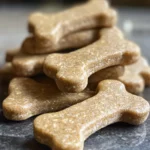 Bone-shaped homemade peanut butter oat dog treats stacked on a kitchen counter
